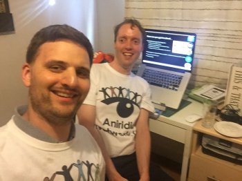 Two men wearing Aniridia Network UK t-shirts and a laptop showing a webinar in progress